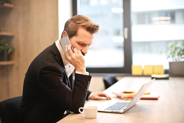 a person talking on the phone while using a laptop