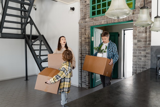 a small family carrying boxes into an open floor plan