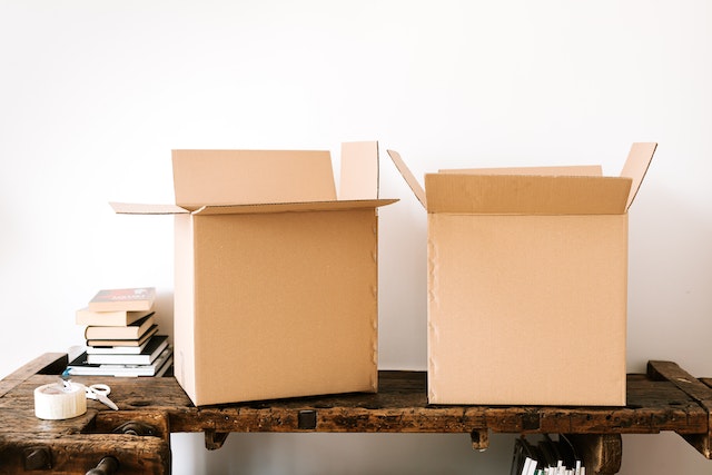 two cardboard boxes on a desk next to books and tape