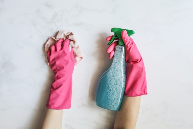 hands with pink gloves holding cleaning supplies