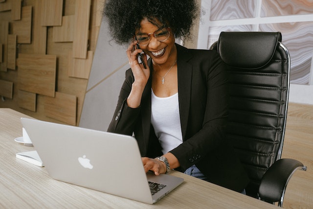 smiling person at a laptop speaking on the phone